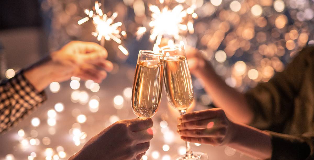 Vier Personen stoßen vor festlichem Hintergrund mit Sekt an und halten Wunderkerzen in der Hand