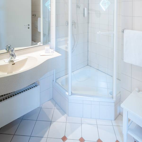 Ein weiß gefliestes Badezimmer mit Duschkabine und Waschbecken in einem Hotel auf Amrum.