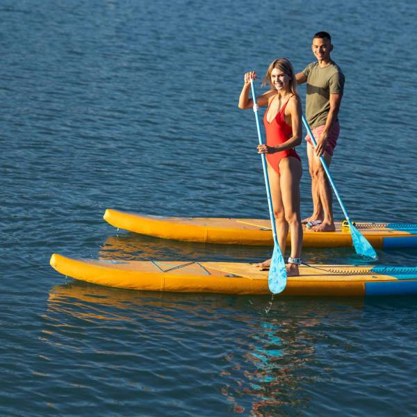 Mann und Frau paddeln nebeneinander auf gelben SUP-Boards auf einem stillen Gewässer