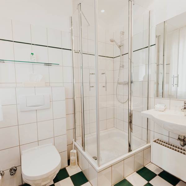 Ein Badzimmer im Hotel Hüttmann mit dunkelgrün weißen Fliesen auf dem Boden.