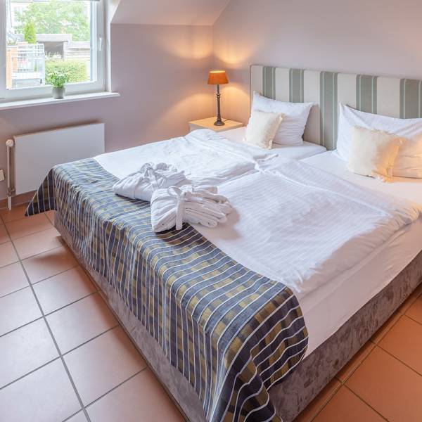 Ein gemachtes Doppelbett mit Bademänteln darauf in einer Suite im Hotel Hüttmann auf Amrum.