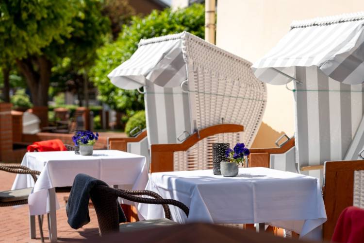 Terrasse des Hotel Hüttmanns mit weißen Strandkörben, gedeckten Tischen und Blumen in der Sonne auf Amrum