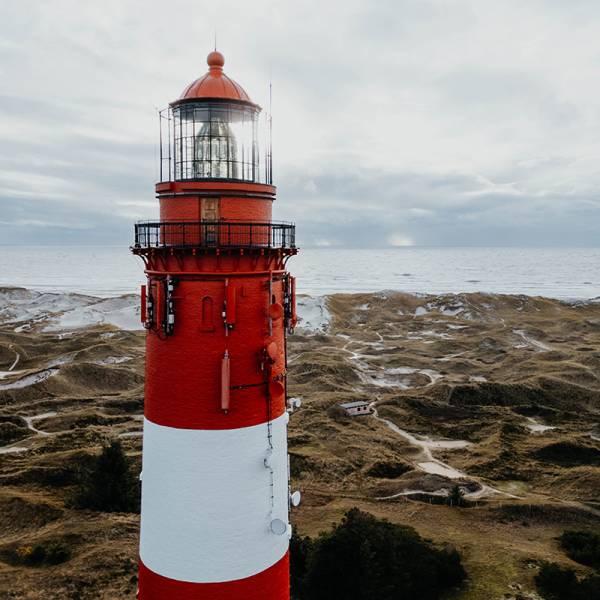 Ein rot-weißer Leuchtturm in den Dünen an der Nordsee an einem wolkigen Tag.
