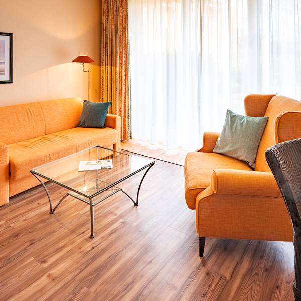 Eine orange Couch und ein dazu passender Sessel stehen an einem Glastisch im Hotel Hüttmann.