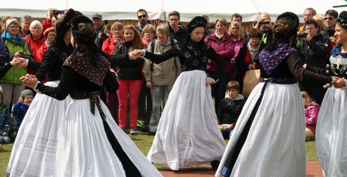 Eine Trachtengruppe mit 5 Frauen tanzt im Vordergrund, Zuschauer sind im Hintergrund.