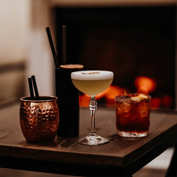 Verschiedene schlichte Cocktails auf einem Holztisch vor einem Kamin.