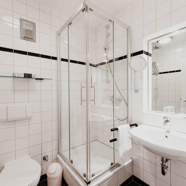 Ein weiß gefliestes Badezimmer mit Duschkabine, Waschbecken und schwarzen Akzenten in einem Hotel auf Amrum.