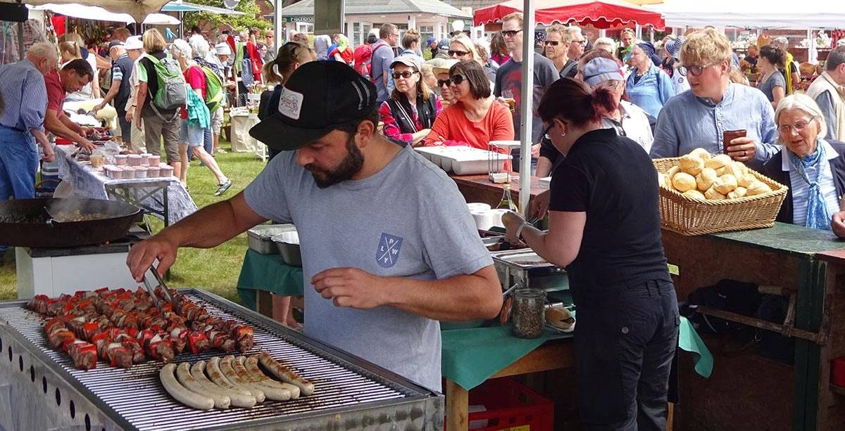 Grillstand auf einem gut besuchten Markt mit Fleischspießen, Bratwürsten und Menschen in der Warteschlange