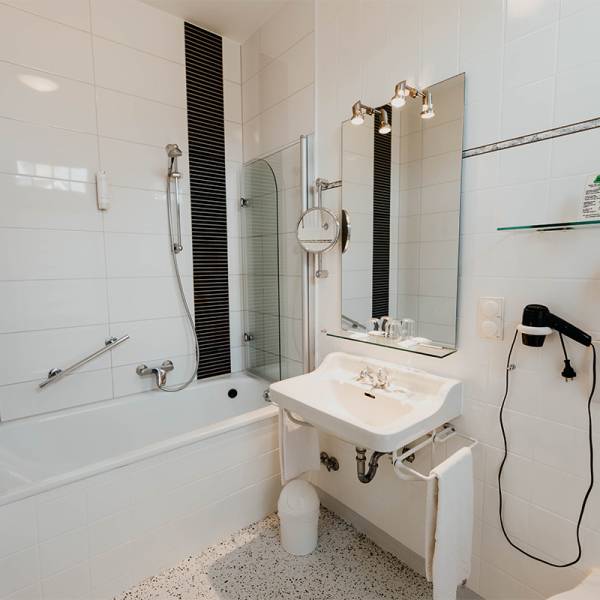 Ein Badezimmer mit weißen Fliesen, einer Duschwanne und Waschbecken in einem Hotelzimmer.