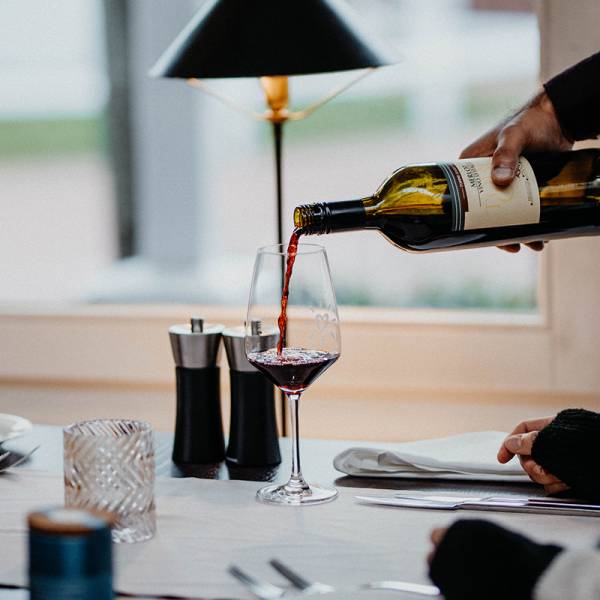 Eine Person schenkt ein Glas Rotwein an einem Tisch in einem Restaurant ein.