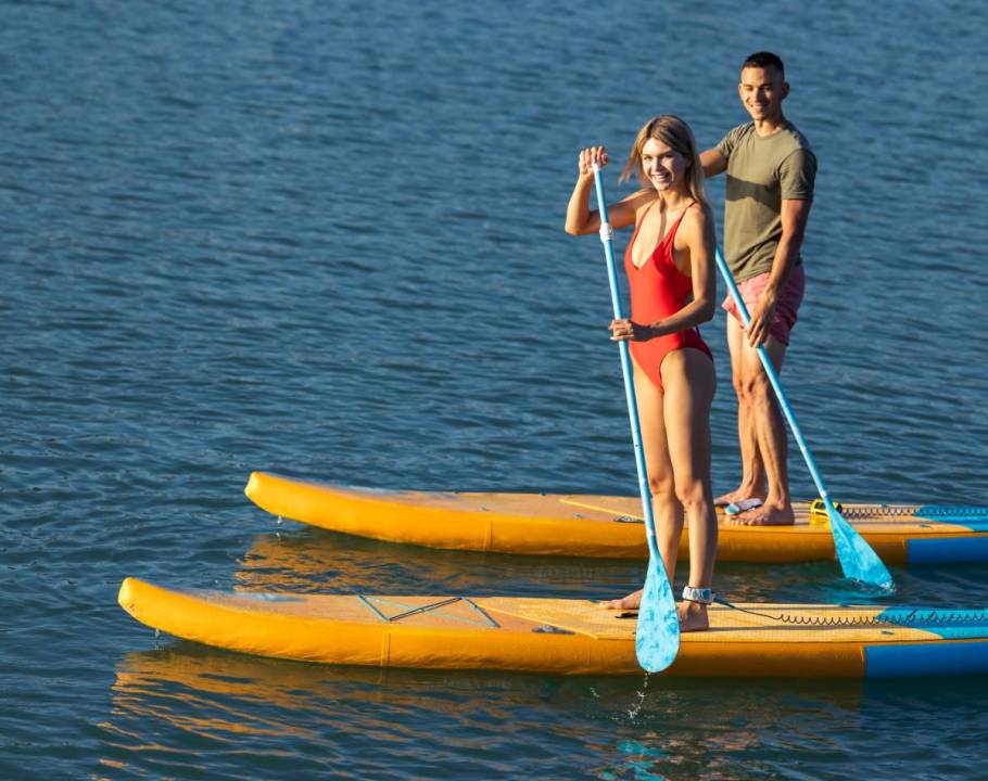 Mann und Frau paddeln nebeneinander auf gelben SUP-Boards auf einem stillen Gewässer