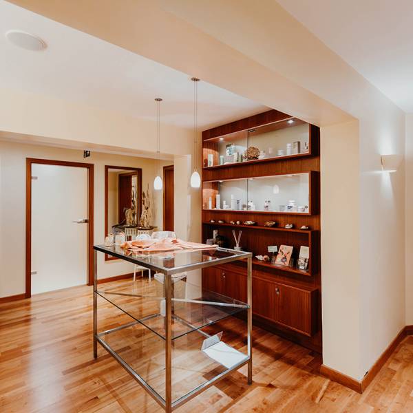 Ein Regal aus dunklem Holz bestückt mit verschiedenen Kosmetikprodukten, davor ein hoher Tisch aus Glas.