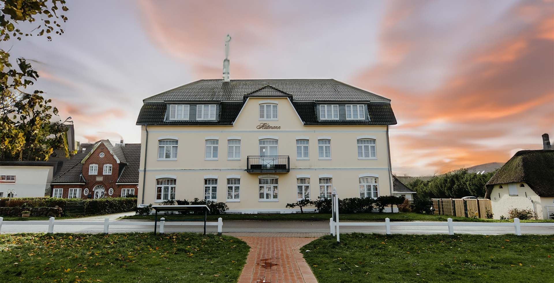 Außenansicht des traditionsreichen Hotel Hüttmann auf Amrum mit heller Fassade bei Sonnenuntergang.