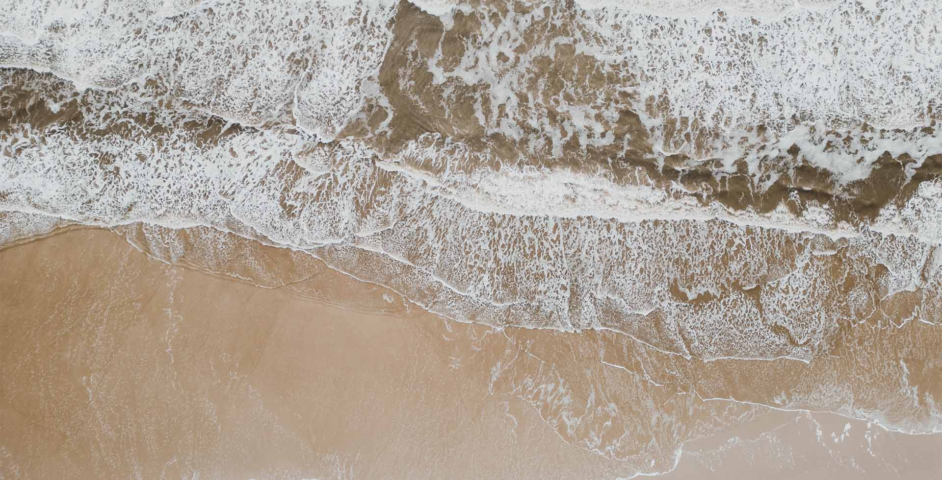 Luftaufnahme von sanften Wellen, die an den Sandstrand der Insel Amrum spülen.